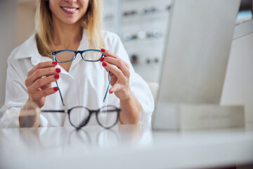 Elegant charming female in white blouses choosing new lenses for eyeglass in ophthalmology clinic