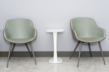 Front view of modern, simple chairs with white table against grey wall in a minimal style, waiting room interior. Chairs in waiting room of doctor's office with copy space for text