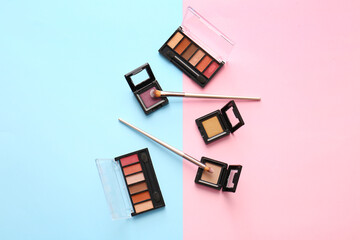 Beautiful palettes of eyeshadows and brushes on color background