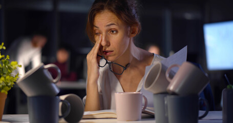 Executive woman overworking having several cups of coffee on desk at night office