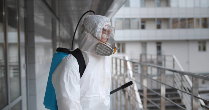 Worker wearing hazmat suit disinfecting terrace in office building