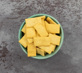 Top view Cheese and garlic snack crackers in a green bowl on a gray mottled background.