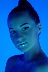 Fototapeta premium Glowing. Handsome woman's portrait isolated on blue studio background in neon light, monochrome. Beautiful female model. Concept of human emotions, facial expression, sales, ad, fashion and beauty.