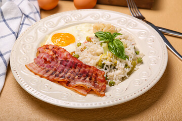 Plate with tasty egg, bacon and rice on color background