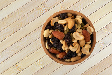 Assortment of nuts and dried fruit in a wood bowl atop a wood placemat top view.
