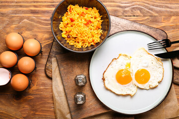 Plate with tasty eggs and rice in bowl on wooden background