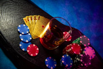 The game chips lie on the table next to a glass of alcohol on a black wooden surface. Game chips for betting in gambling. Poker chips. Playing cards.