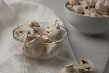 Sliced and whole fresh mushrooms in bowls on a white tablecloth