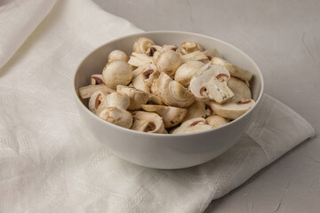 Whole and chopped mushrooms in a round porcelain bowl on a white towel