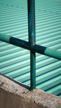 Cruz de barrotes met&aacute;licos verde claro y oscuro en barandilla junto a techo de uralita verde cobalto