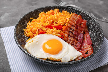 Plate with tasty egg, bacon and rice on dark background