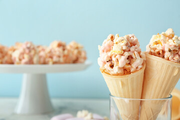 Waffle cones with popcorn balls in glass on color background