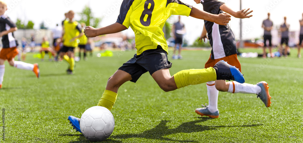 Wall mural Young african soccer player running fast and kicking white football ball. Youth footballers compete in tournament match. Soccer athlete kicking ball. School sports competition