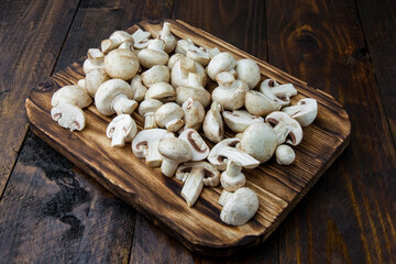 A burnt cutting board with fresh whole and sliced champignons on a dark wooden background