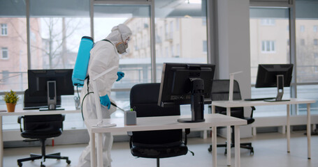 Person in white hazmat suit disinfecting office to prevent covid-19