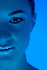 Close up woman's portrait isolated on blue studio background in neon light, monochrome. Beautiful female model. Concept of human emotions, facial expression, sales, ad, fashion and beauty.