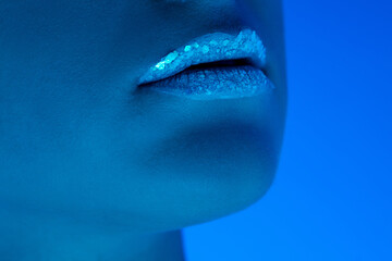 Close up female lips and cheeks isolated on blue studio background in neon light, monochrome. Beautiful female model. Concept of human emotions, facial expression, sales, ad, fashion and beauty.