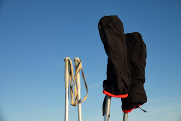 Attributes of a ski trip. Ski poles and mittens on a blue sky background. Halt