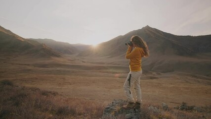 Side view of female photographer holding camera in hands and photographing wild nature and mountains at sunset 