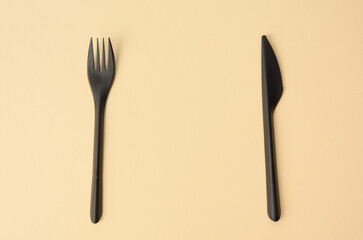 disposable black plastic fork and knife on a brown background, close up, set, copy space