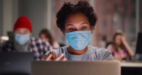 Mixed race woman wearing face mask sanitizing hands at desk in office.
