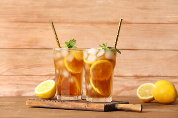 Fototapeta premium Glasses of cold black tea with lemon on wooden background