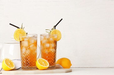 Glasses of cold black tea with lemon on light background