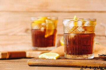 Glasses of cold black tea with lemon on wooden background