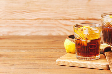 Glass of cold black tea with lemon on wooden background