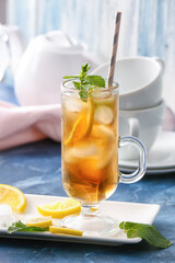Cup of cold black tea with lemon on color background
