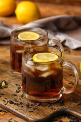 Cups of cold black tea with lemon on wooden background