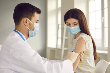 Male nurse or doctor in medical face mask giving flu injection to female patient during seasonal...