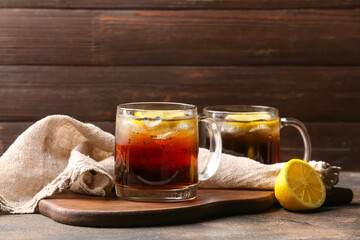Cups of cold black tea with lemon on wooden background