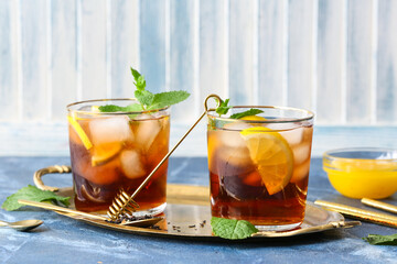 Glasses of cold black tea with lemon on color background