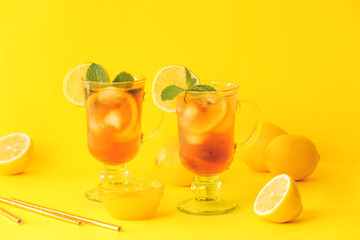 Cups of cold black tea with lemon on color background