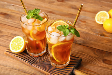 Glasses of cold black tea with lemon on wooden background