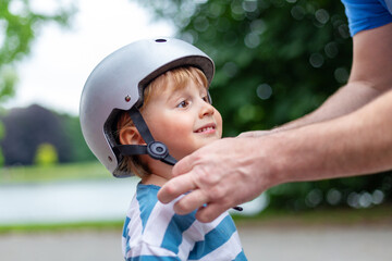 Fototapeta na wymiar Father puts a safety helmet on little smiling boy for scooter ,cycling and rollerblading in the park. child safety on the playground