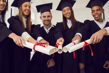 Multiethnic group young happy university graduates friends joining diplomas together as symbol of...