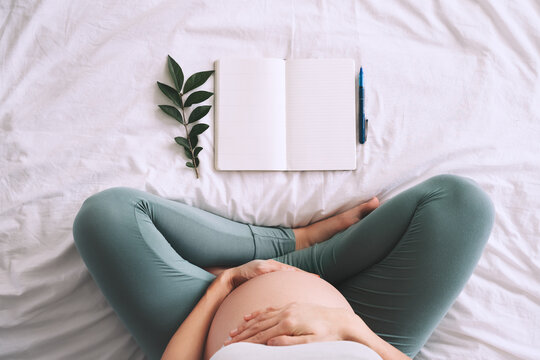 Pregnant woman with beautiful belly makes notes or check list in paper diary. Concepts of preparation for baby birth, tips for a healthy pregnancy.