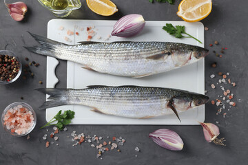 Two raw mullet with ingredients and seasonings on white plastic board on dark background. Top view
