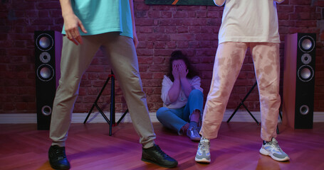 Upset young woman sitting near wall watching people dancing in dance studio