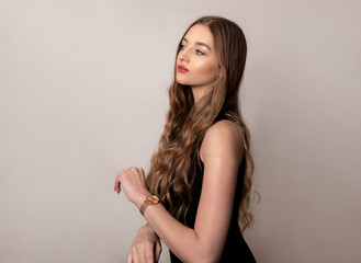 Beautiful young woman with long and healthy wavy hair posing in dress showing healthy figure and wearing wrist watch