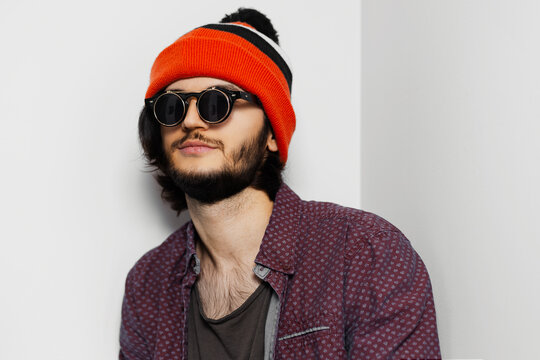 Studio portrait of young guy wearing round sunglasses and orange hat on white background.