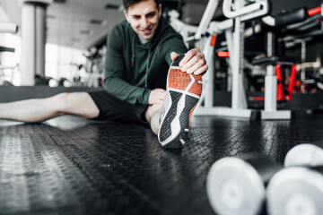 Close up focus of male athlete on the floor reaching for the tip of his leg, stretching before training. Sports lifestyle