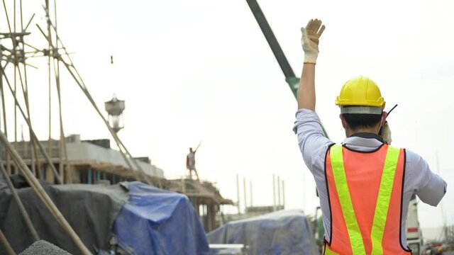 asian asian foreman in hard hat  talking by walkie talkie control crane and concrete bucket Pouring cement with worker outdoors on construction site. contractor using radio operation in industry