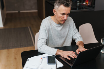 Serious grey man working with laptop while sitting in living room