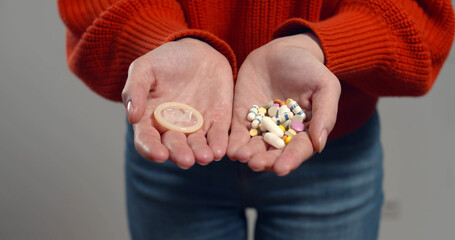Close up of woman holding birth control pills and condom isolated on grey background
