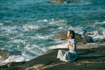 A young yoga woman meditates in the lotus position sitting on the ocean coast.