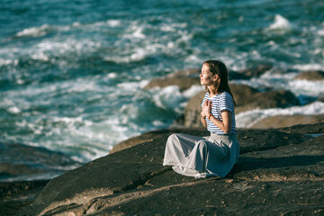 Yoga woman sitting on rocks on the ocean coast.