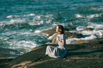 Young woman sitting on rocks on the the sea beach. Yoga and fitness.